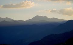A scenic view of layered blue and gray mountains under a soft sky with scattered clouds.