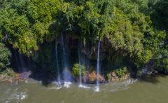 A lush waterfall cascades into a river, creating a rainbow in the mist.
