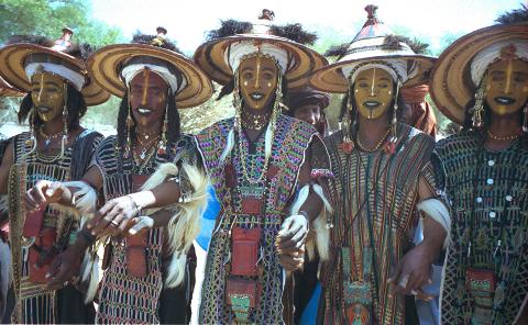 A group of men with painted faces and traditional hats and clothing stand together, possibly during the Cure Salée festival.