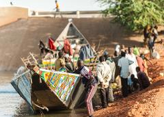 A group of people are gathered around a colorful boat on the edge of a body of water.