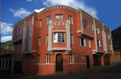 Here's a description of the image:A three-story corner building with a salmon-colored facade and white architectural details is seen under a blue sky.