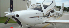 A white Cirrus SR22 airplane with its distinctive gull-wing doors open is parked on the tarmac.