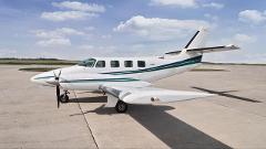 A white and green twin-engine aircraft sits on a concrete runway under a partly cloudy sky.