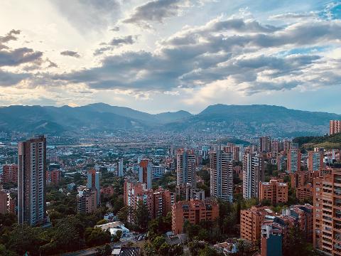 A cityscape with tall buildings and mountains in the background under a cloudy sky.