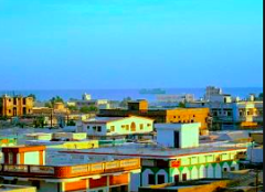 Here's a description of the image, keeping it within the character limit:A panoramic view shows a coastal city with boxy, colorful buildings under a clear blue sky, and the ocean visible in the background.