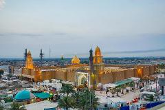 An aerial view captures a large, illuminated building with golden domes and minarets amidst a bustling city at dusk.