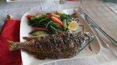 A whole grilled fish is served with green beans, carrots, and a lemon wedge on a white plate with a red napkin and silverware on the side.