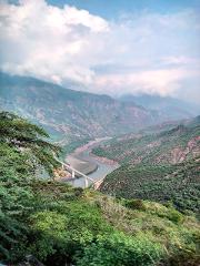 A scenic view of a river winding through mountains with a bridge spanning across it, captured on a cloudy day.