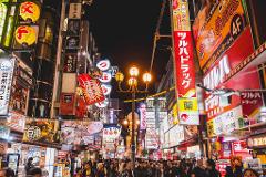 A vibrant night scene in Osaka, Japan, showcases bustling streets lined with colorful signs and crowded with pedestrians, creating a lively and exciting atmosphere.