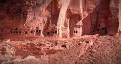 A rock face featuring small, carved doorways in its surface, possibly tombs or dwellings, suggesting an ancient site in a desert or arid region.