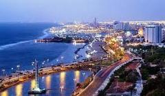 Here's a description of the image:This is an aerial view of Jeddah, Saudi Arabia at dusk, showing the coastline, city lights, and modern architecture.