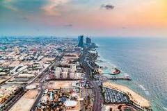 Here's a description of the image:An aerial view captures a sprawling coastal city with modern architecture, highways, and a vibrant waterfront bordering the sea under a colorful sky.