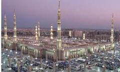 Here's a description of the image:The image shows a large mosque at dusk, illuminated with lights and surrounded by many people.