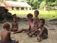 Five children sit outside a building in Papua New Guinea, some smiling at the camera.