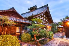 A serene Japanese temple stands majestically, its traditional architecture complemented by lush greenery and a stone pathway under a twilight sky.