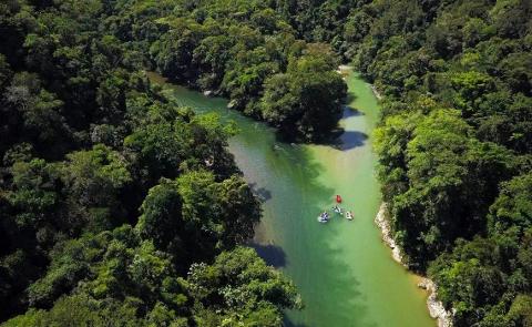 Aerial shot of lush rainforest surrounding a river with a group of people rafting down it.
