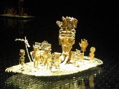 Gran Tour incluyendo Bogotá, Medellín, Nuquí y Valle del Cocora - 11 Días A detailed golden Muisca raft artifact with figures and an elaborate central figure, displayed on a reflective surface against a dark background.