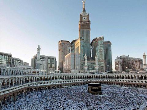 A wide-angle shot captures the Grand Mosque in Mecca, Saudi Arabia, with the Kaaba surrounded by worshippers, set against a backdrop of modern skyscrapers including the iconic Abraj Al-Bait clock tower.