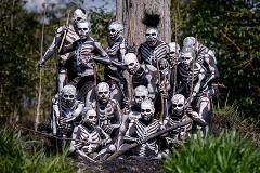 A group of men from the Skeleton Tribe are gathered together, wearing intricate white skeleton paint on their black bodies, holding sticks, and posing in front of a tree in the highlands of Papua New Guinea.