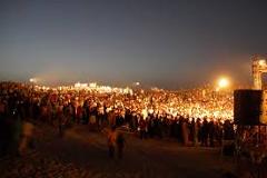 Here's a description of the image:A large crowd gathers under the night sky, illuminated by stage lights, possibly at the Agadez African Music Festival or Festival Au Desert.