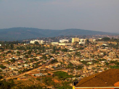 Ein Überblick über eine Stadt in Ruanda oder der Demokratischen Republik Kongo mit Gebäuden, Häusern und Bäumen, eingebettet in eine hügelige Landschaft unter einem dunstigen Himmel.