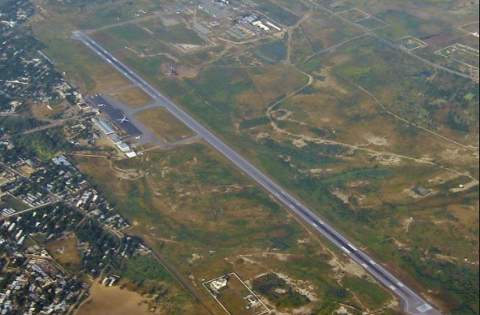 An aerial view captures an airport runway surrounded by sparse vegetation and buildings.