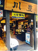 Her er en beskrivelse af billedet: En japansk restaurant med en traditionel træfacade, der viser skilte på japansk, og kunder der bliver betjent indenfor.