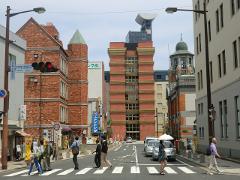 A street scene in Japan shows people crossing a zebra crossing with various buildings and businesses visible.