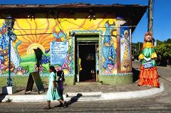 A colorful building with cat-themed murals and a mannequin wearing a traditional dress, with two women walking by.