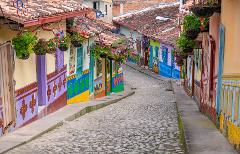 A vibrant street scene in Guatapé, Colombia showcases colorful buildings adorned with hanging plants, set against a cobblestone street that leads the eye down a gently curving path.
