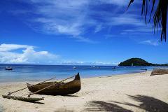 A traditional wooden canoe rests on a sunny sandy beach with a backdrop of a blue sky and ocean.