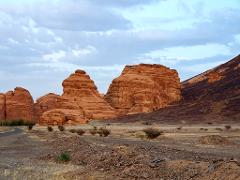 A picturesque desert landscape features unique rock formations and a rugged terrain, with a cloudy sky overhead.