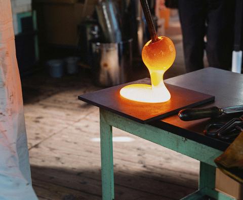 A glowing orange blob of molten glass is being shaped on a dark surface during a glass crafting workshop.