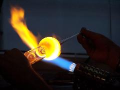 A glassblower shapes molten glass with a torch and tools in a crafting workshop, creating art with fire.