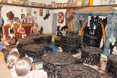 Peuples et civilisations des Grassfields Un groupe de touristes assis et regardant une pièce décorée d'objets tribaux, notamment des tables en bois sculpté, des chaises et des œuvres d'art.