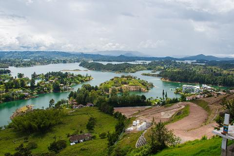 An expansive view of a lush, green landscape dotted with islands in a lake, under a cloudy sky.