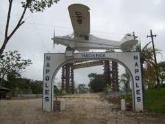 Here's a description of the image:The entrance to Hacienda Nápoles is marked by an arch topped with a white airplane, under which a path leads into the estate.