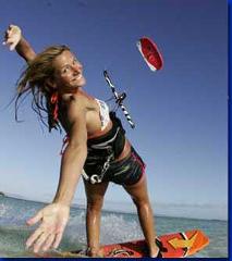 Here is a description of the image:A woman is kitesurfing in the ocean, smiling with one arm raised, while her board is visible under her feet.