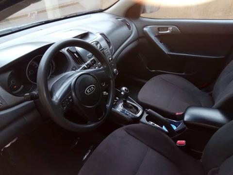 The image shows the interior of a Kia car, focusing on the steering wheel with the Kia logo, dashboard, seats, and center console.