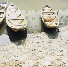 The image shows several small boats docked along a muddy shoreline with debris, suggesting a riverbank scene likely from Kano.
