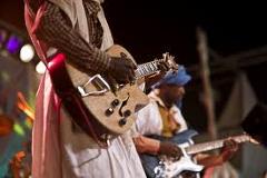 Two musicians are playing electric guitars during a performance at a festival, with colorful stage lights visible in the background.
