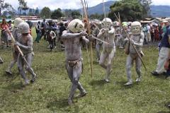 A group of men in tribal masks and body paint march across a grassy field with bows and arrows, as part of the Goroka Show Festival in Papua New Guinea.