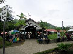 A bustling scene at the Rabaul Page Park Market, featuring people, stalls, and signage under overcast skies.
