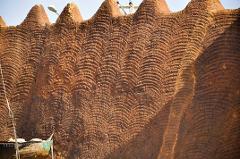 A wall of a traditional mud building, adorned with wave-like patterns in brown tones, possibly found in Kano.