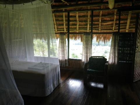 This is an interior shot of Karawari Lodge, showing a room with a bed draped in mosquito netting, a chair, and windows overlooking a green landscape.