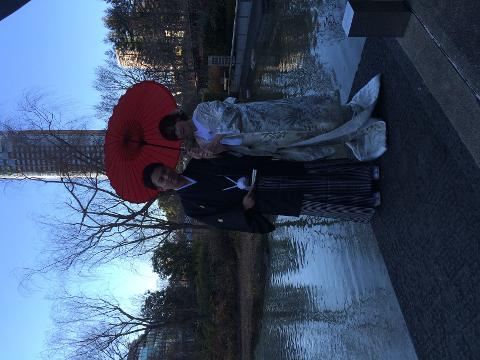 Traditional Japanese Wedding Ceremony & Kimono Experience – 1-Day Tokyo Tour A couple in traditional Japanese wedding attire stand by a pond under a red umbrella.