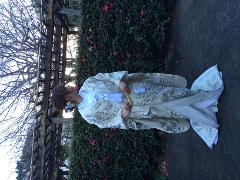 Traditional Japanese Wedding Ceremony & Kimono Experience – 1-Day Tokyo Tour A woman in a traditional white kimono stands beside a flowering bush and a wooden trellis, likely during a Japanese wedding ceremony or cultural experience.