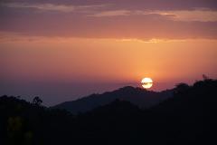 A mesmerizing sunset with a vibrant orange sun dipping behind silhouetted mountain ranges under a sky painted with hues of purple and orange.