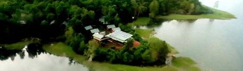 Aerial view of Lake Murray Lodge surrounded by lush green trees, with a lake reflecting the sky, offering a serene and natural setting.