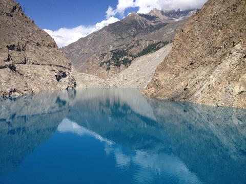 A stunning turquoise lake reflects towering rocky mountains under a blue sky with fluffy white clouds.